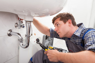 Jack Plumbing technician repairing leaking drain pipes under sink